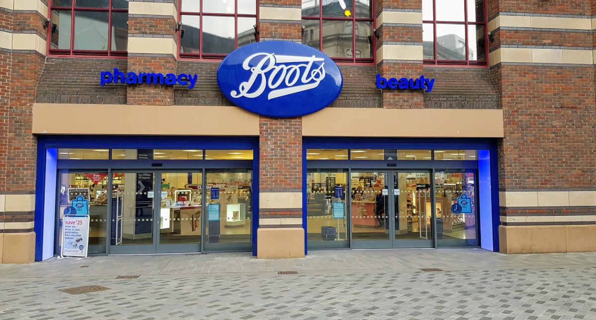 Blue aluminium shopfront with automatic sliding entrance doors at a Boots pharmacy