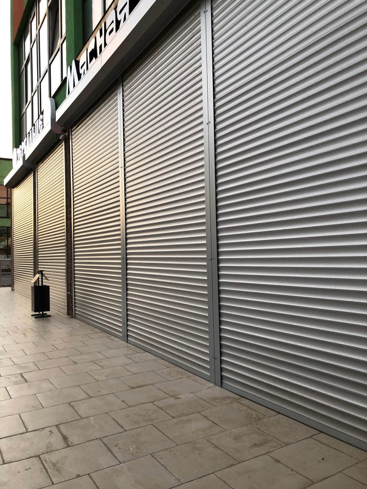 Galvanised solid security roller shutters closed across a row of retail units